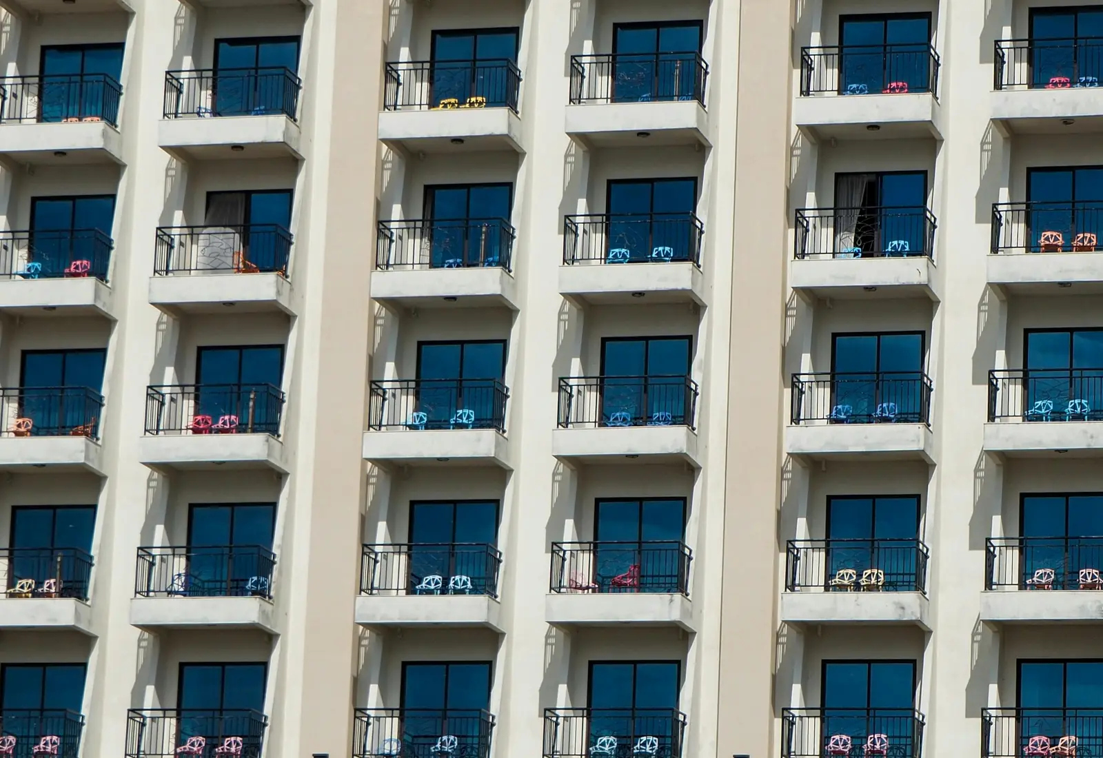Rows of identical hotel balconies on a cream facade, each with a pair of colored chairs
